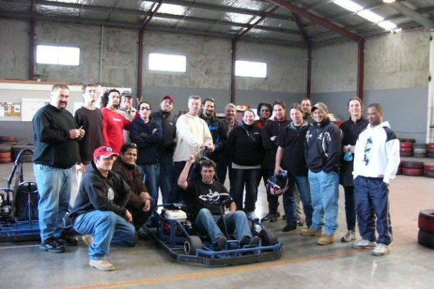 Group of people posing with go-karts in an indoor track.