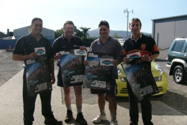 Four men holding posters, standing outside near cars and a building.